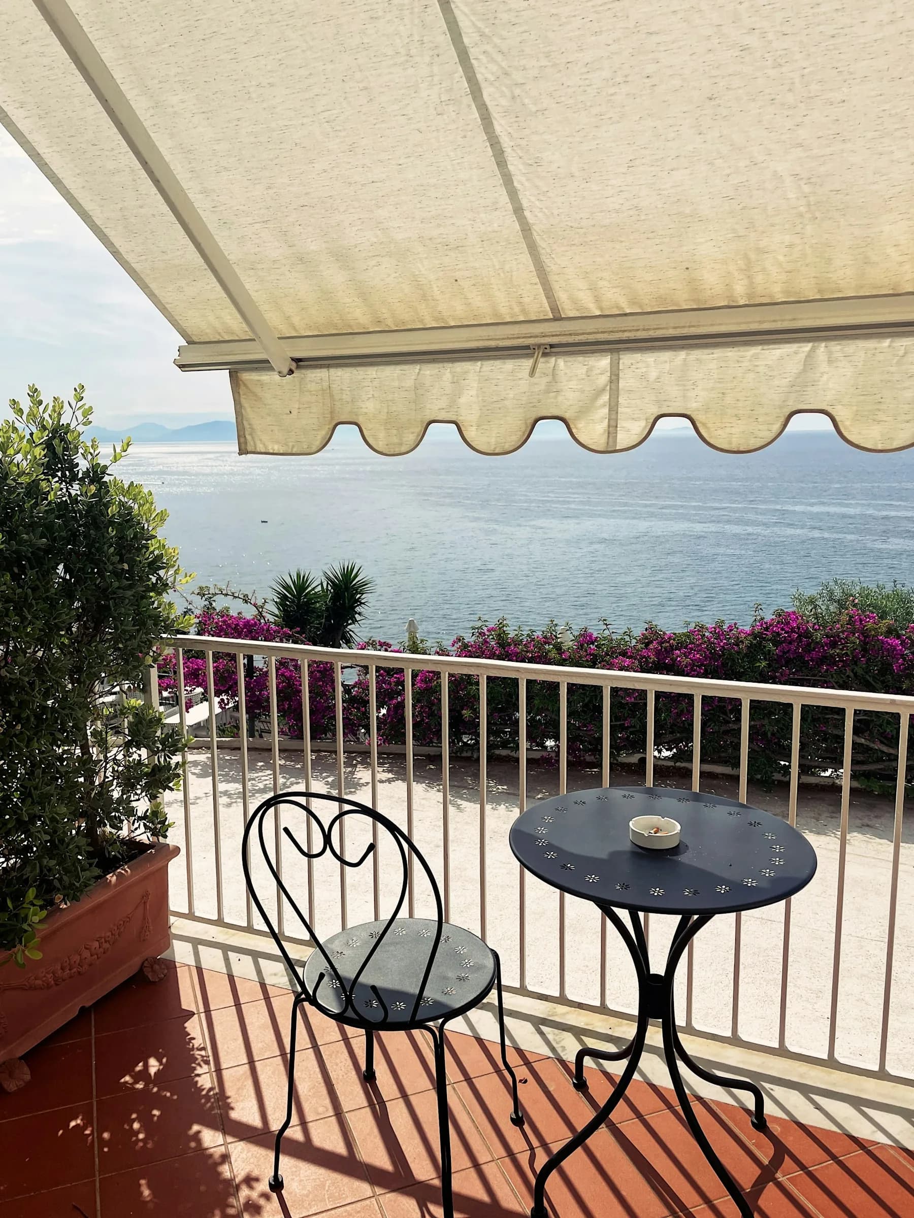 Una terrazza con tavolino e sedie di ferro sotto la tenda, affacciata sul mare